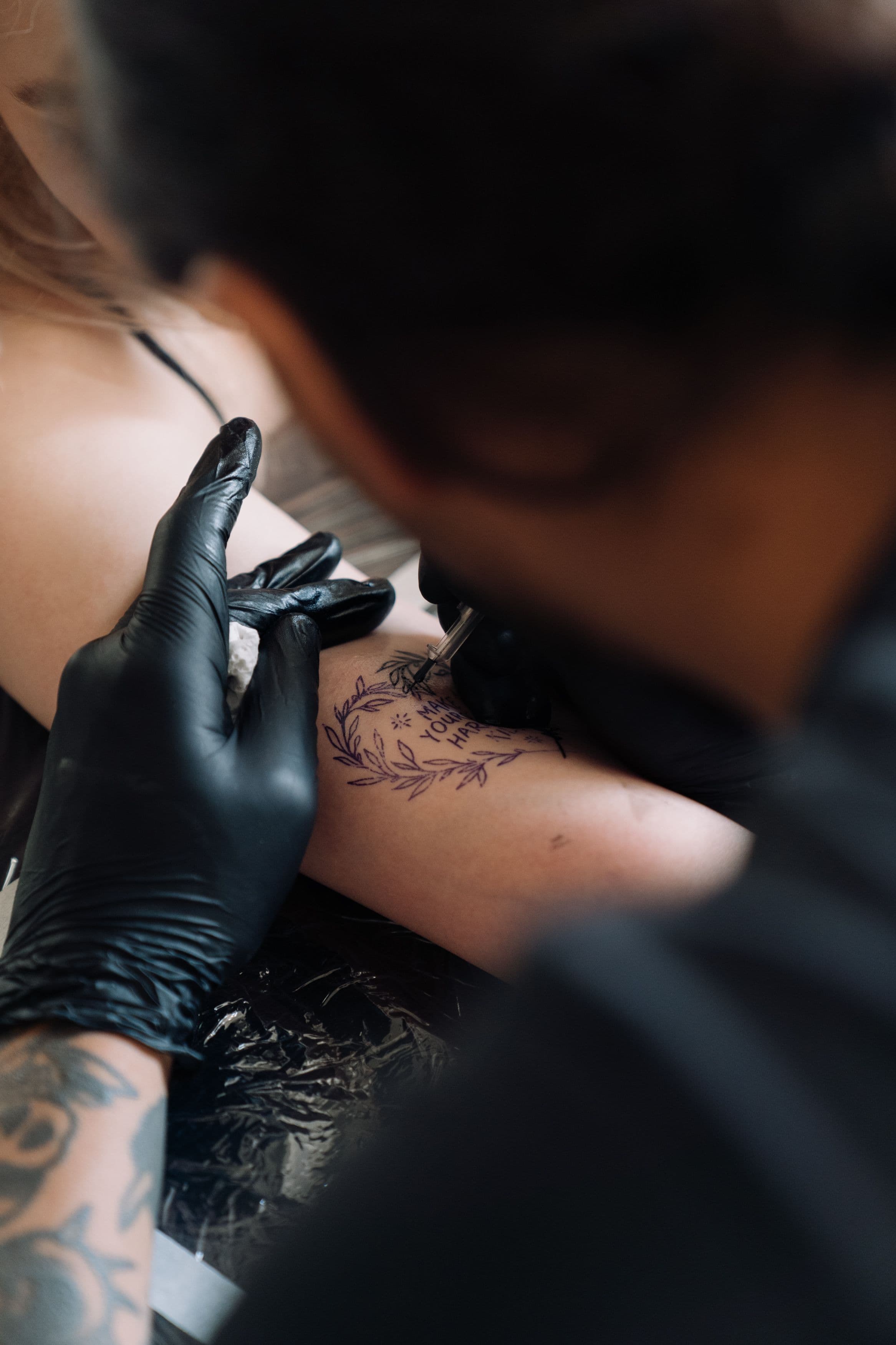 Tattoo artist inking a laurel and quote design